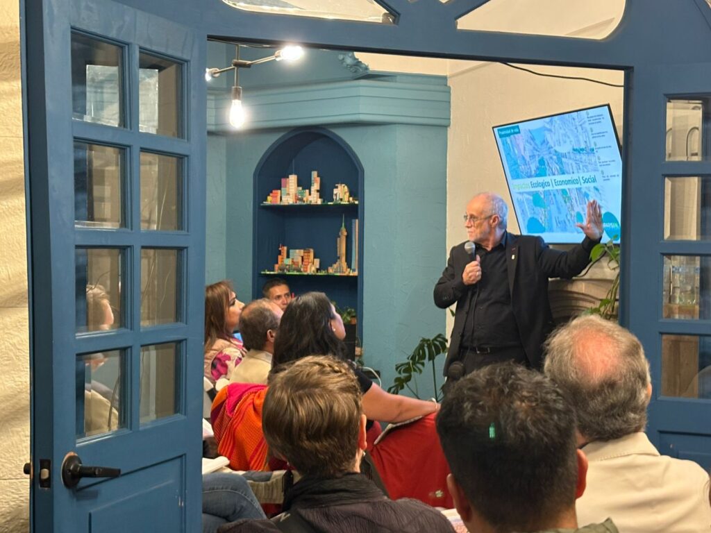 Fotografía del panel o de la tertulia: Carlos Moreno, legisladores y especialistas en mesa de diálogo con imagen institucional del Colegio de Urbanistas de México al fondo.